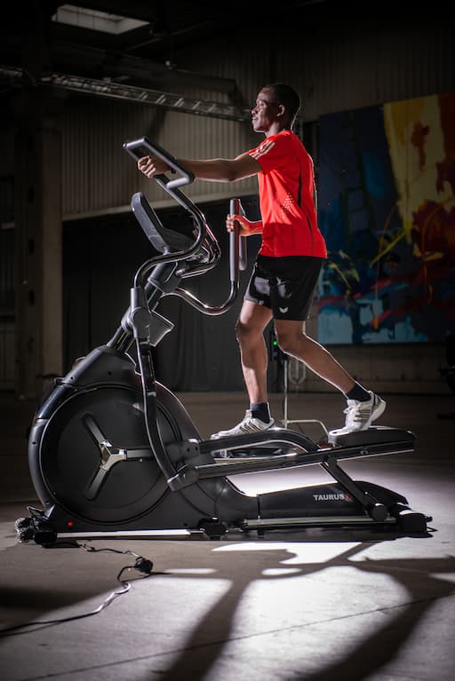 Person in Sportkleidung trainiert auf dem Taurus FX10.5. Das Ger&auml;t steht in einer dunklen Halle und ist mit einem Spotlight ausgeleuchtet.