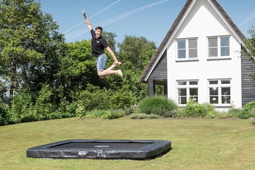 Person springt auf einem InGround Trampolin in einem Garten.