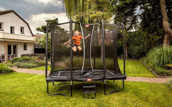 Kind springt auf einem Berg Trampolin in einem Garten.