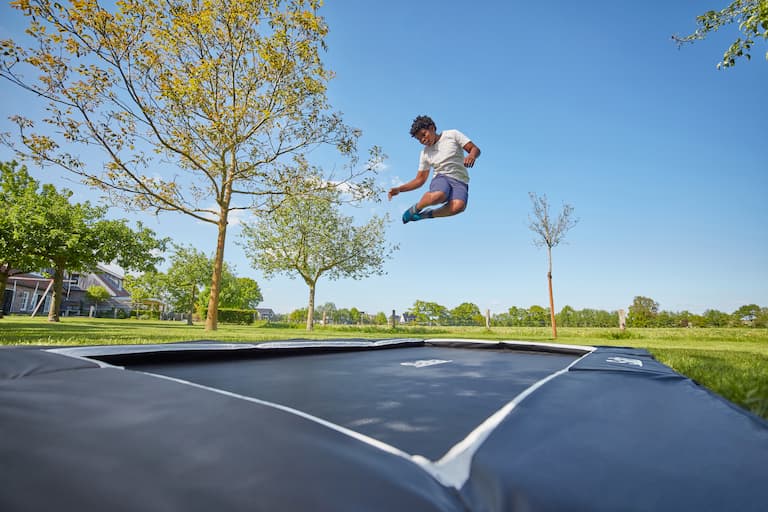 Ein Kind springt auf einem rechteckigen Trampolin im Garten, welches im Boden eingegraben ist. 