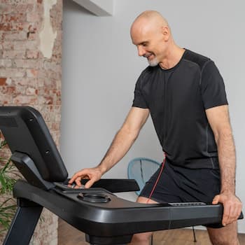 Eine Person steht auf einem Laufband und nimmt Einstellung an den Bedienelementen vor. Mit einer Hand fasst sie locker an den Handlauf des Laufbands. 