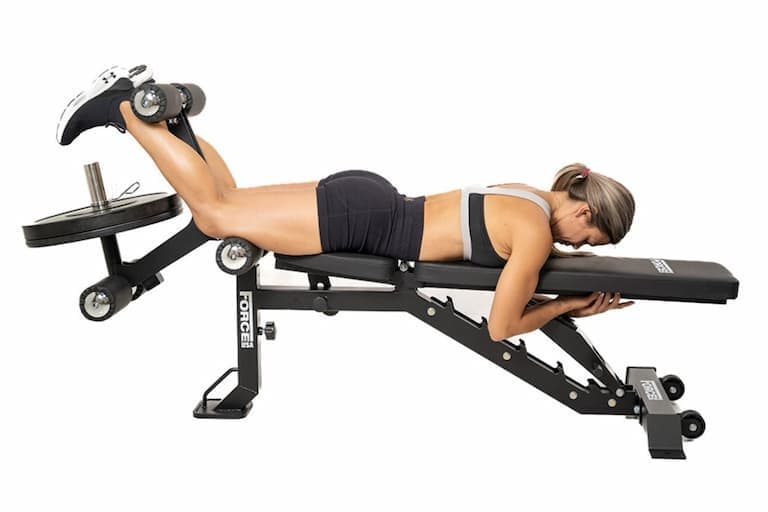 Person in sportlicher Kleidung führt eine Beincurl-Übung an der Force USA Hantelbank MyBench FID aus.