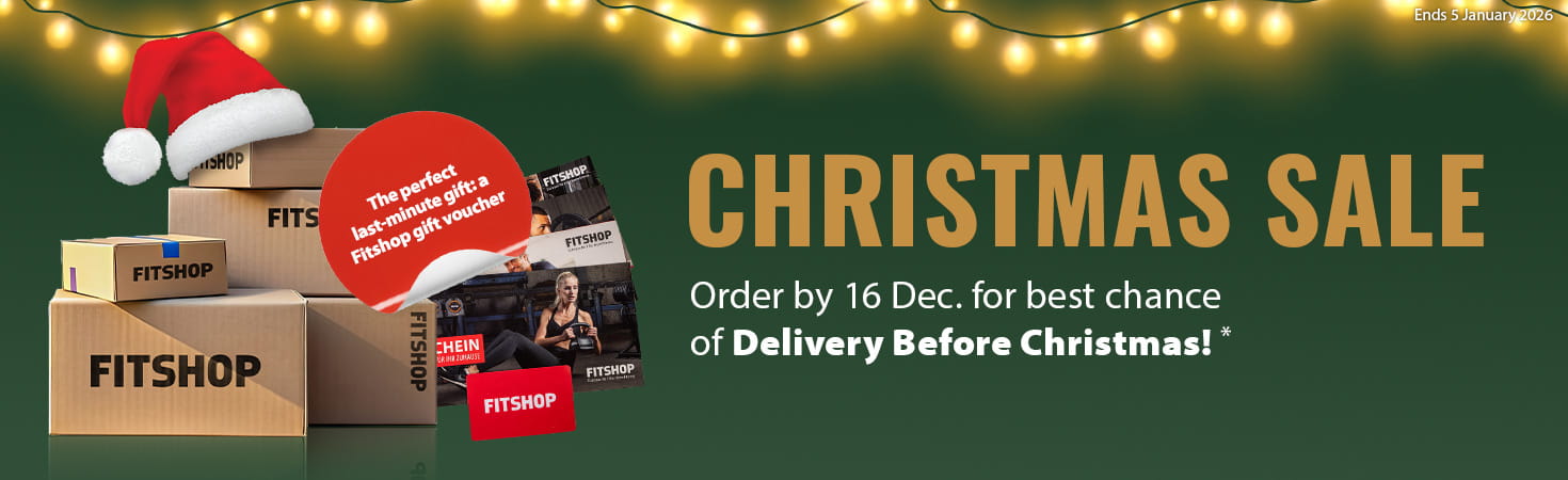 A Christmas ad banner with green background and a string of lights along the top border. On the left side are many packages labelled “Fitshop”. Beside them are multiple gift cards. A red, highlighted text box reads “The perfect last-minute gift: the Fitshop gift card”. On the right side in large letters is written, “Christmas Sale” with the subtext “Delivery before the holidays!”