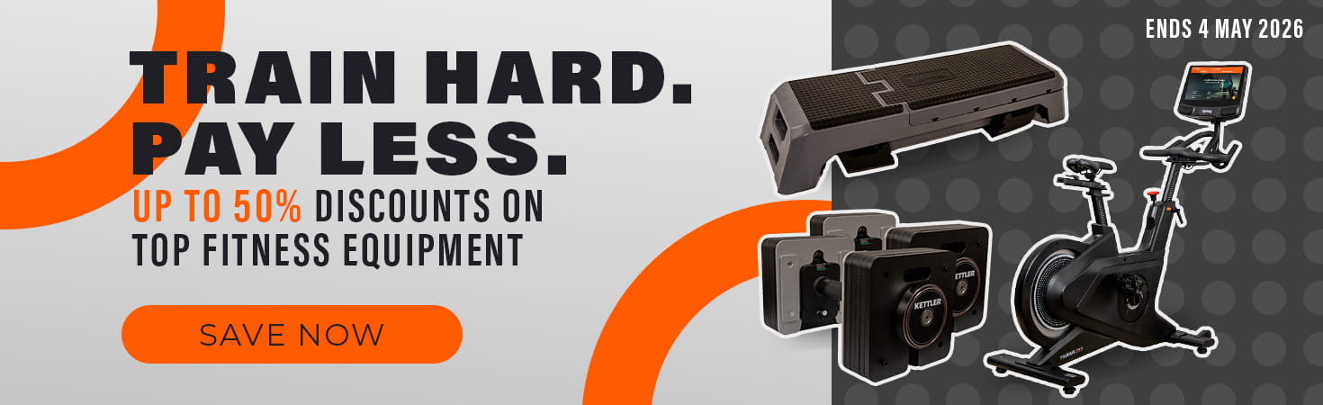 Ad banner in shades of orange and grey. On the right-hand side are a step board, an indoor bike and two dumbbells. On the left side, text reads: „Train hard. Pay less. Up to 50% discounts on top fitness equipment. Ends 4 May 2026. Save now.“