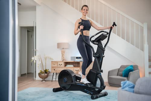 Frau in Sportbekleidung auf einem Crosstrainer im Wohnzimmer