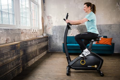 Eine Frau trainiert auf einem Ergometer, das Bild zeigt sie von der Seite