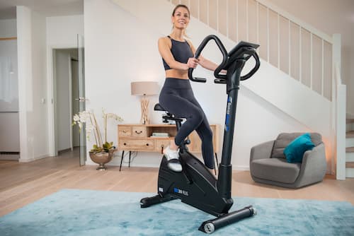 Frau in sportlicher Kleidung auf einem Ergometer in wohnlichem Ambiente