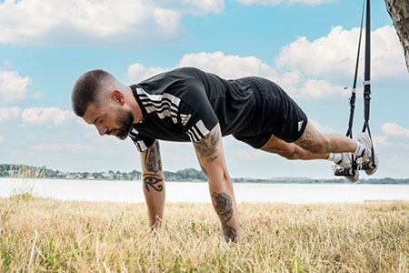 Man in sportieve outfit voert mountain climbers uit op een slingtrainer die buiten aan een boom is bevestigd.