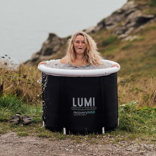 Une femme assise dans un environnement naturel en bord de mer dans un Recovery Pod Max de Lumi, rempli d'eau et de glaçons