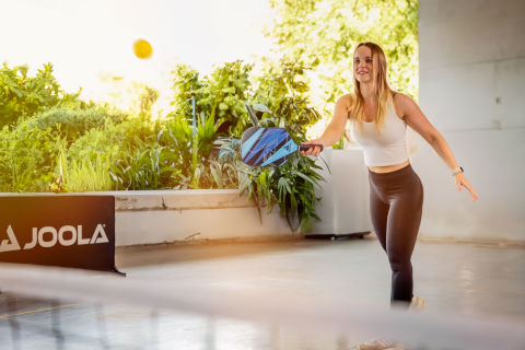 Une femme en tenue de sport joue une balle de pickleball avec une raquette de pickleball par-dessus le filet.