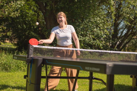 Une femme se tient devant une table de ping-pong et joue.