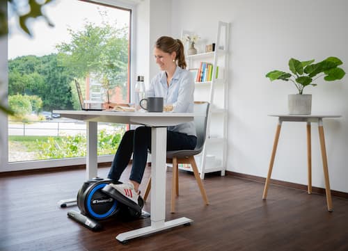 Frau sitzt am Schreibtisch und trainiert mit Mini Stepper