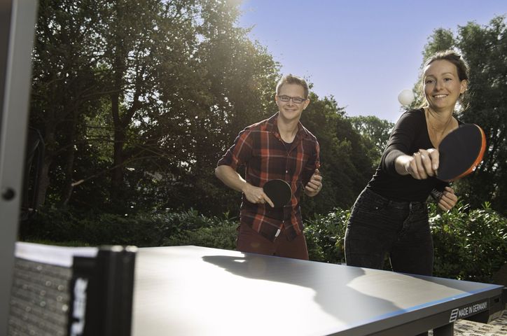 Ein Mann und eine Frau spielen an einer Outdoor-Tischtennisplatte im Garten Tischtennis