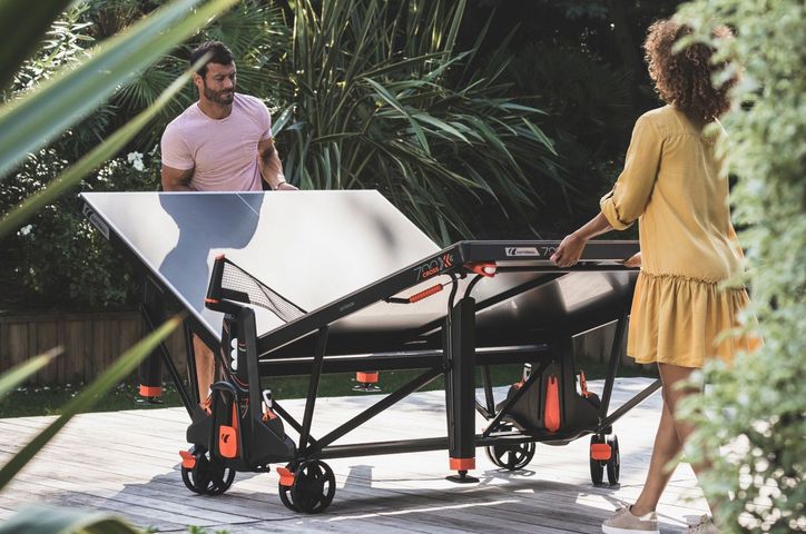 Un homme et une femme plient une table de ping-pong extérieure