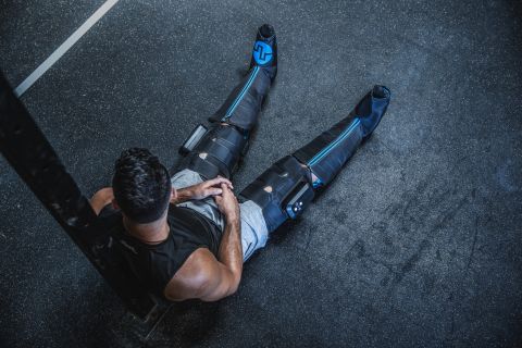 Ein Mann sitzt auf dem Boden nach dem Training und trägt Kompressionsboots.