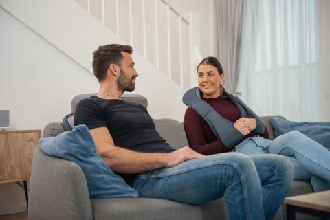 Un homme et une femme sont assis sur un canapé avec un coussin de massage pour cou.