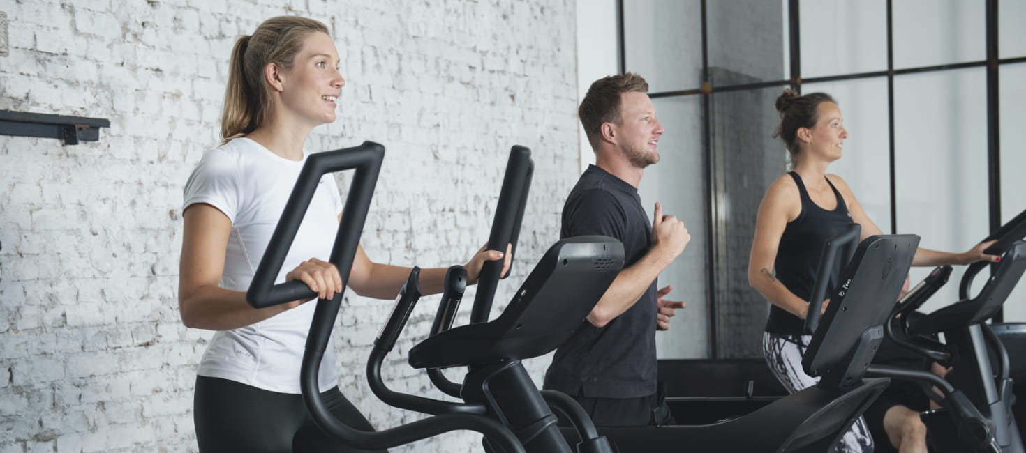 Drei Personen trainieren auf Fitnessgeräten
